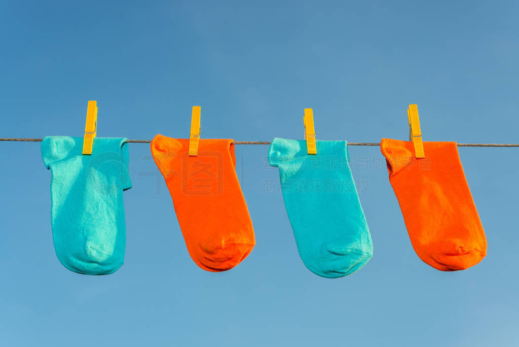 four new, clean, washed blue and orange socks hang on a rope wit