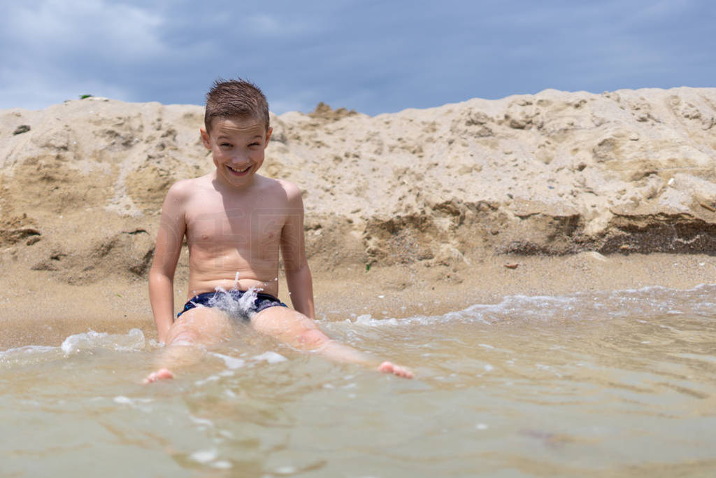 A boy of 9 years old is bathing and resting on a sandy beach by