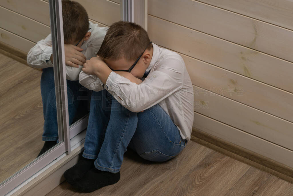 A sad young schoolboy is sitting on the corridor with his hands