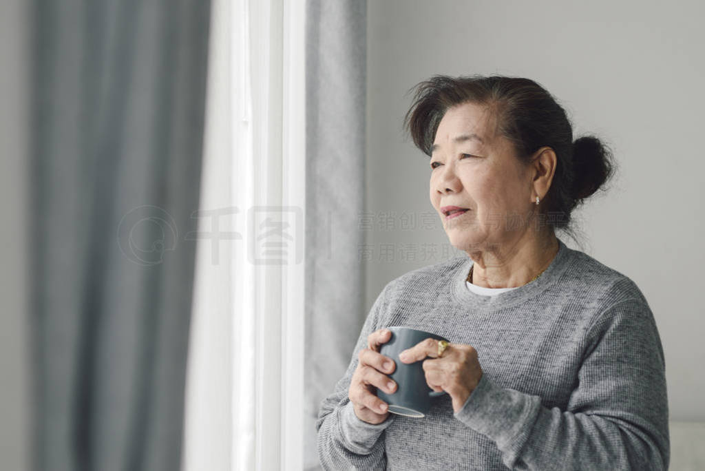 Asian senior woman drinking hot tea near window outdoor, lonely