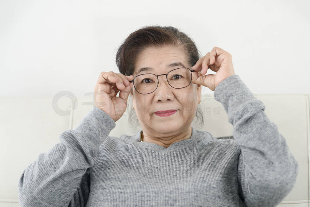 Happy Asian senior woman wearing eyeglasses and sitting on sofa