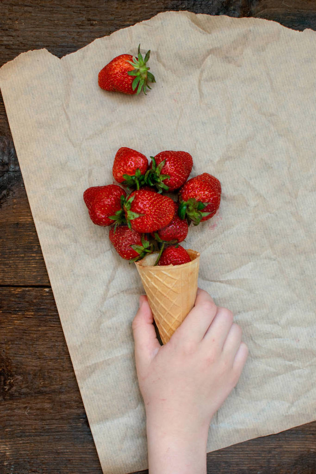 Children's hand takes strawberries in ice cream cone on natural