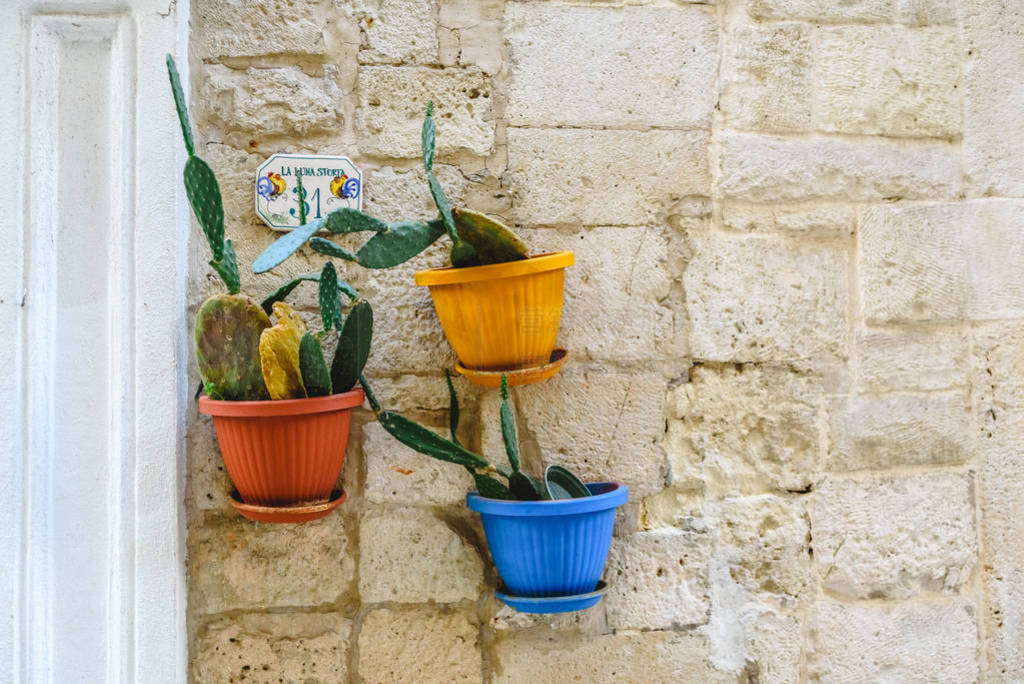 Three flower pots with flowers hanging from the stone facade of