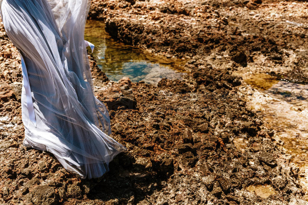 Woman with pink wedding dress on the rocks of the mediterranean