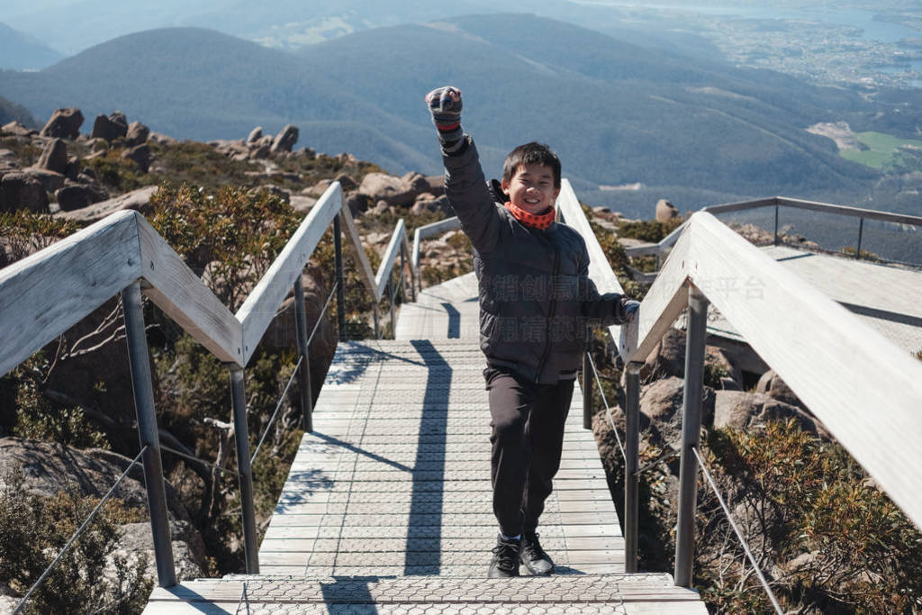 Tween boy standing with hand up on top of the mountain, Preteen