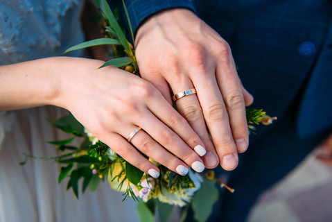 新婚夫婦手牽手展示結婚戒指,特寫.婚禮花束背景上的手和戒指.