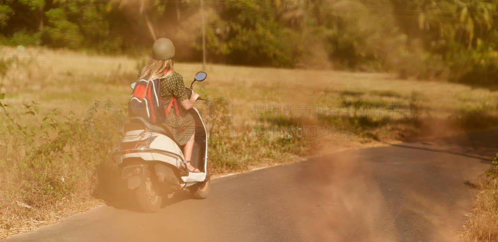 A girl in a green dress drives a scooter.