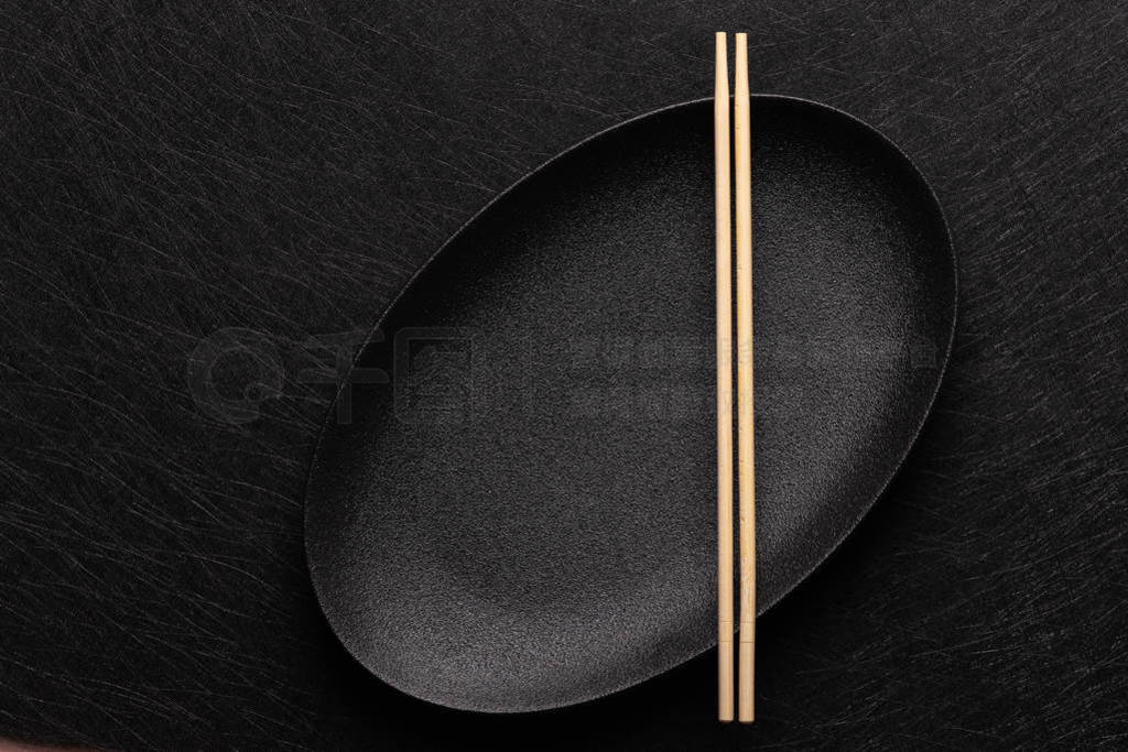 Empty oval black plate with chopsticks on dark background. Japan
