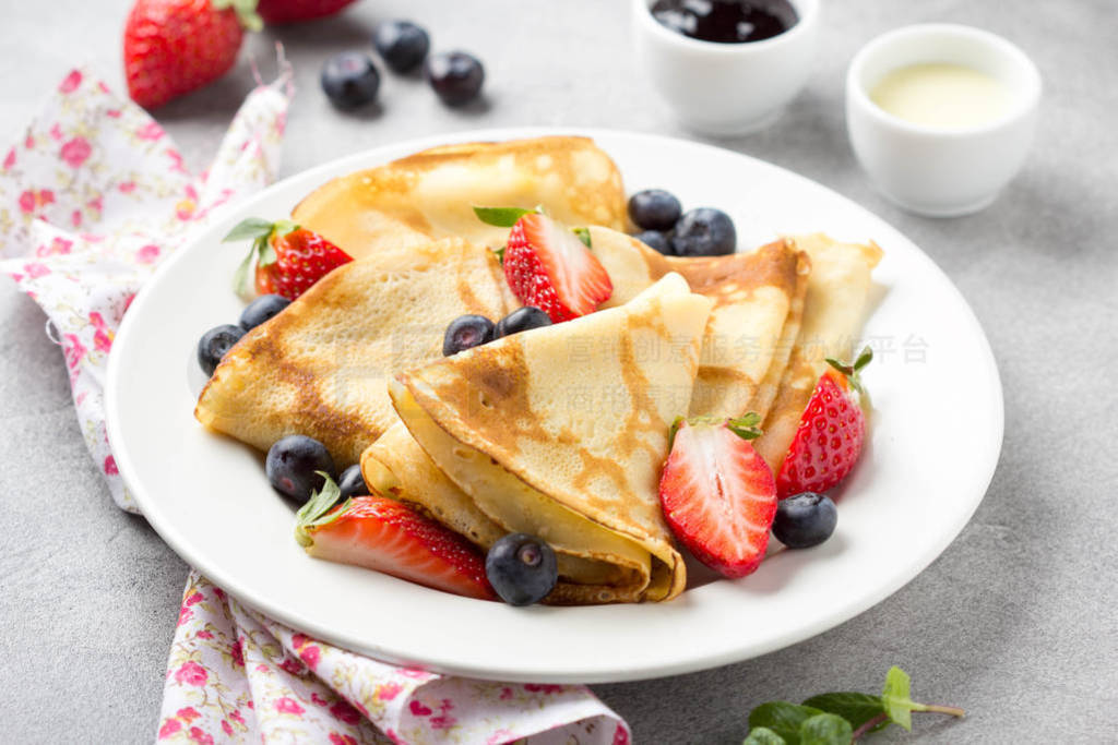 Thin pancakes with strawberries and blueberries, jam, condensed
