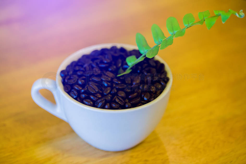 Coffee beans and green leafs in a white cup on a wooden table