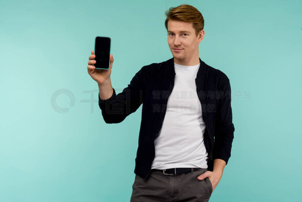 Cheerful sporty red-haired guy shows the smartphone screen on a