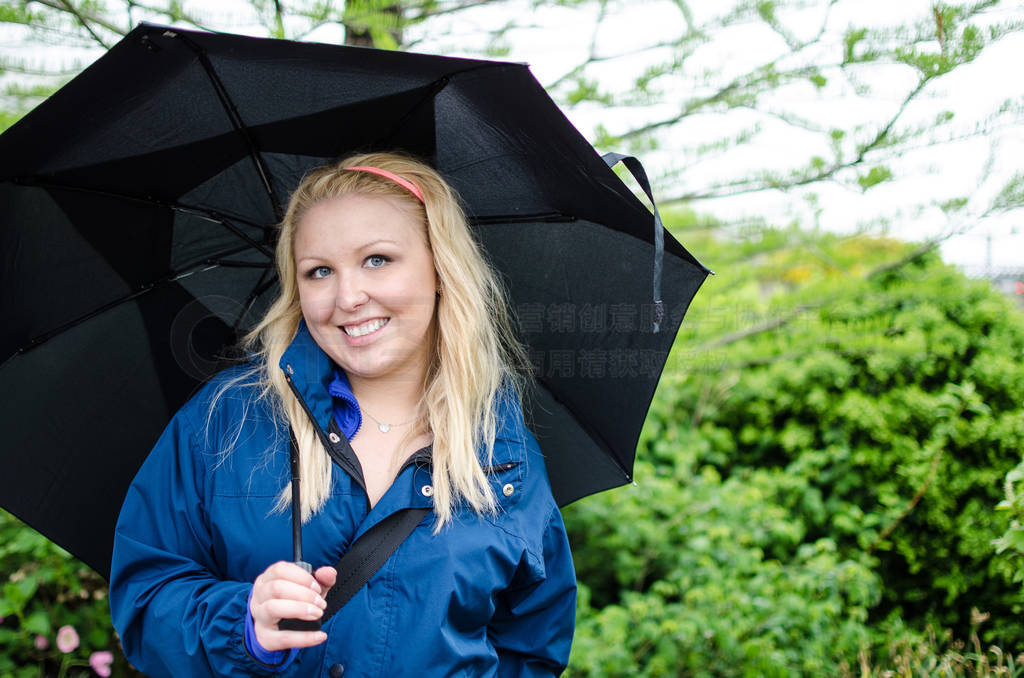 Blonde woman holds a black umbrella on an overcast rainy day in
