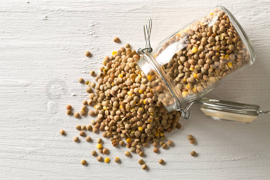 Raw, dry, uncooked brown lentil legumes in glass storage jar on