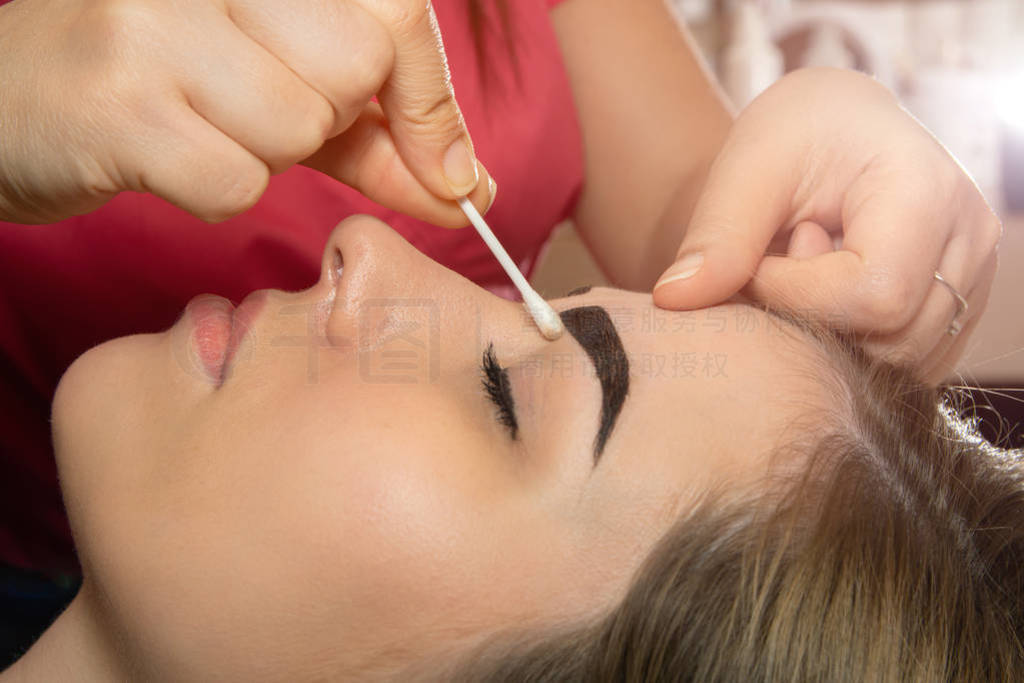 Young woman having professional eyebrow correction procedure in