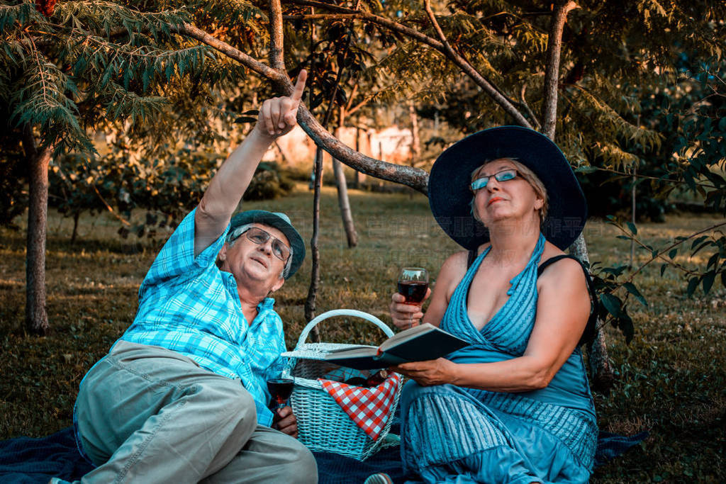 Senior couple pointing away in the sky while drinking wine