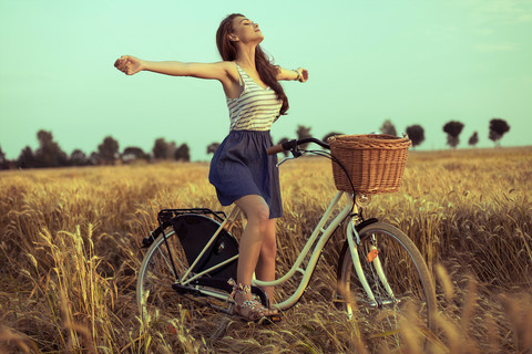 免费女人在日落时享受自由麦田的自行车上