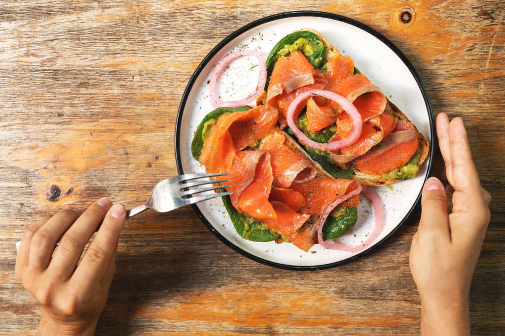 Female hands and delicious toasts with a smoked salmon, avocado