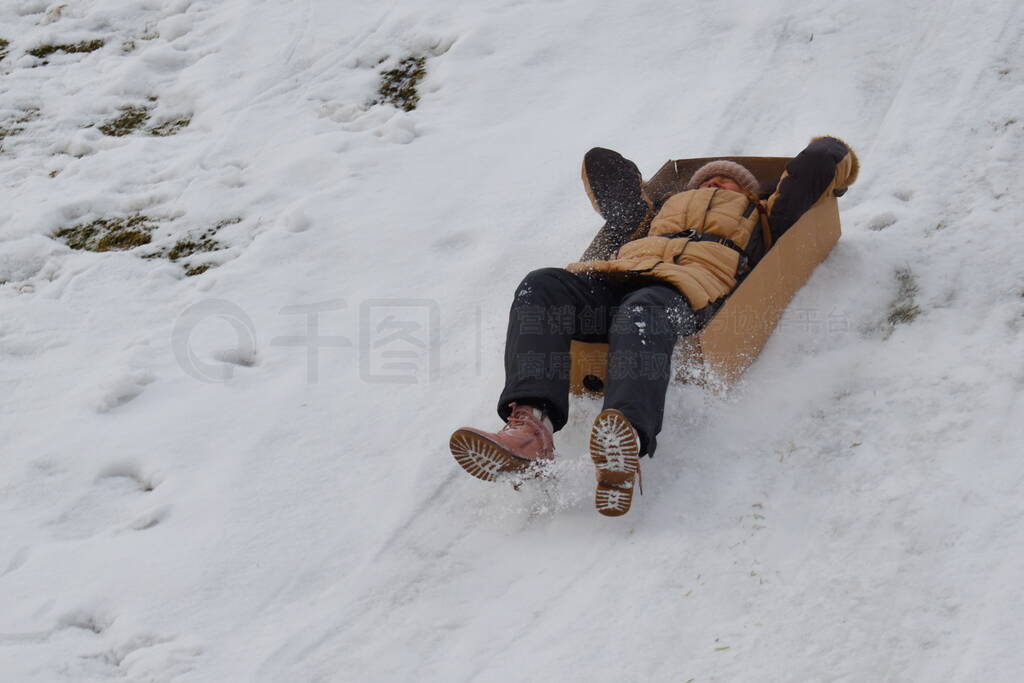 Girl in a cardboard box on hill in winter. Child to have fun in