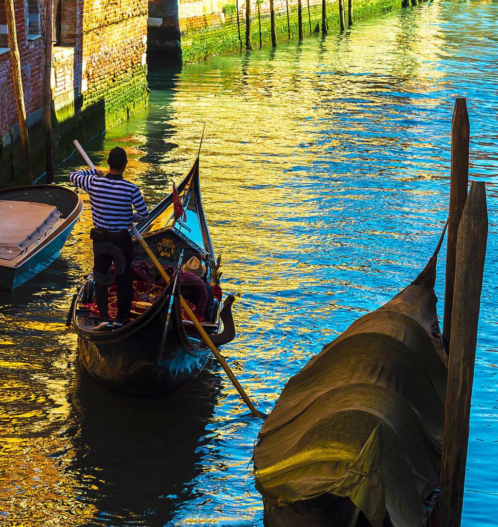 Gondolier rowing on his gondola in a Venetian canal on a summer