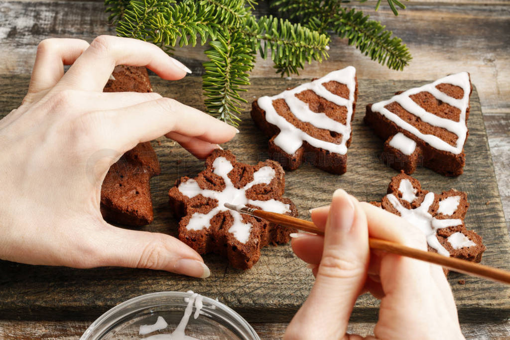 Woman decorating christmas gingerbread cookies in star shape.