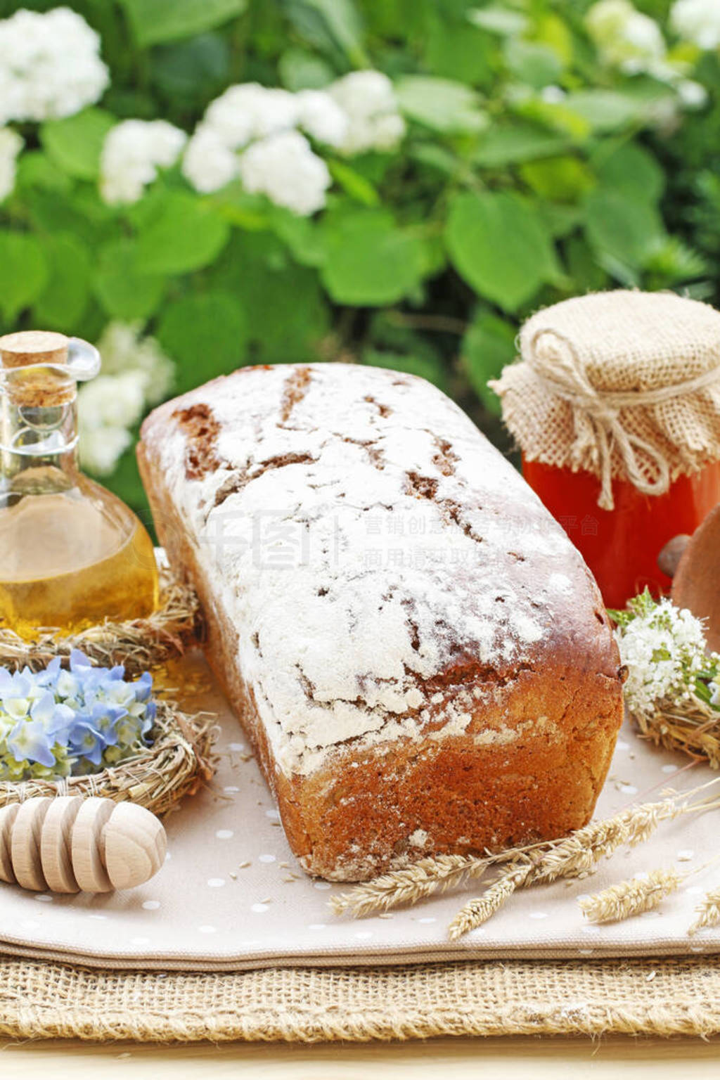 Loaf of bread, jar with honey and summer flowers on the table.