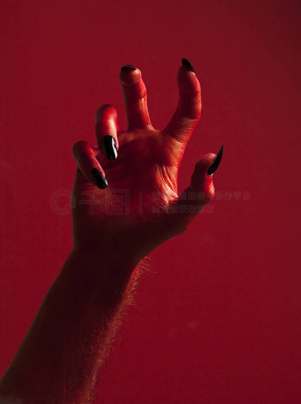 Halloween red devil monster hand with black fingernails against