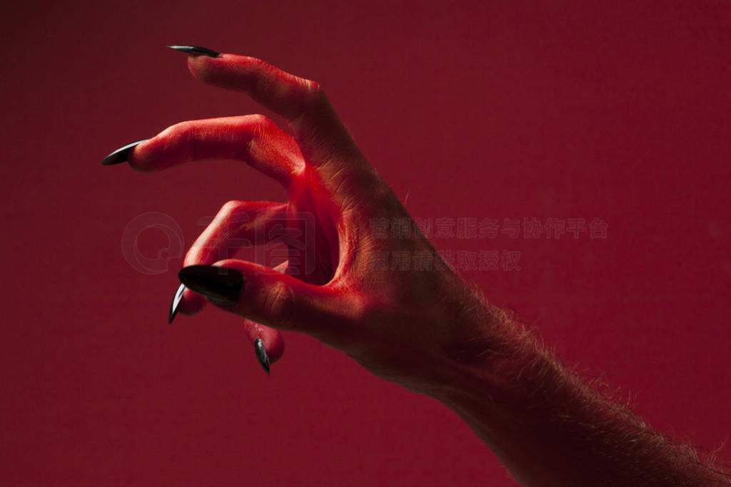 Halloween red devil monster hand with black fingernails against