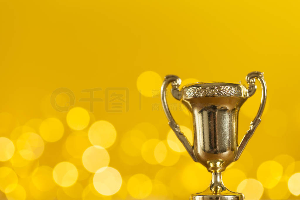 Gold award trophy against bright yellow background with blurred