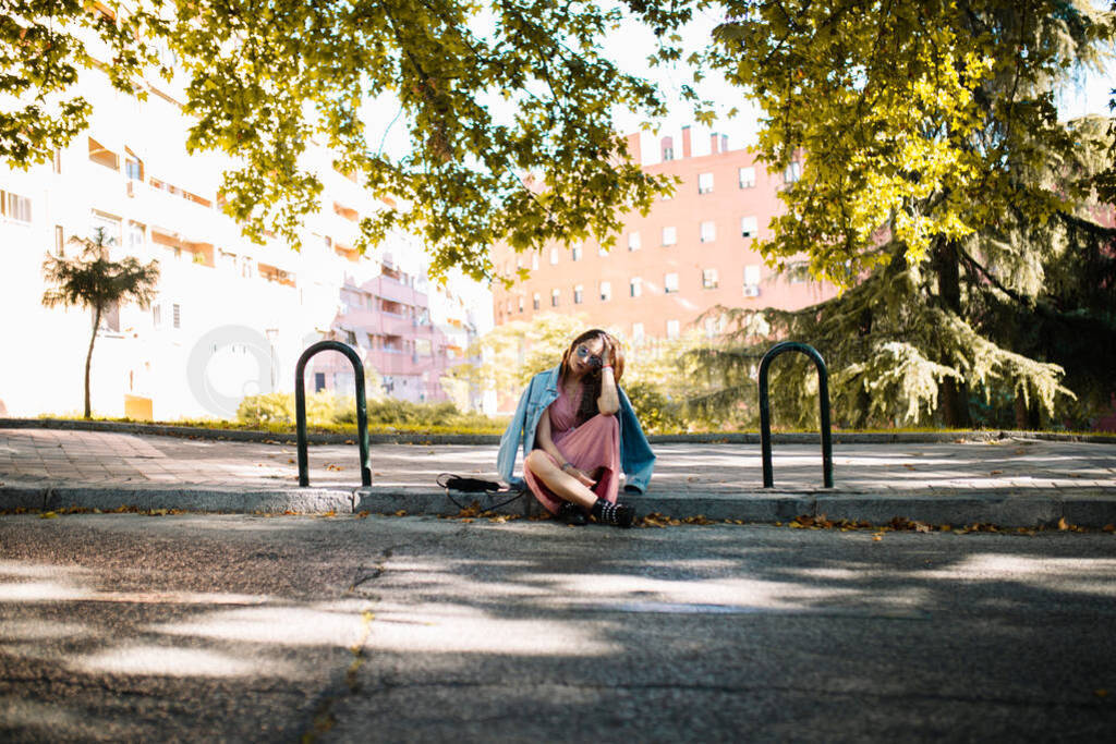 Sad young woman with sunglasses sitting on the sidewalk worried