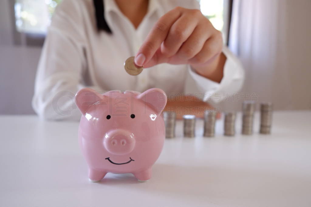 Businessperson Inserting Coins In Piggy Bank With Stack Of Coins