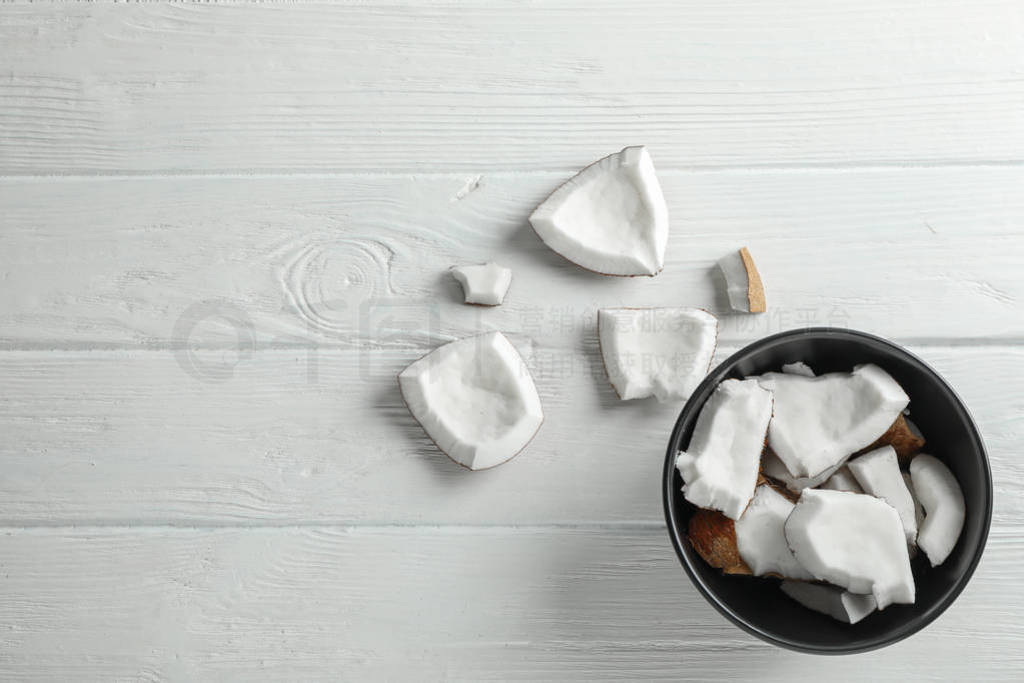 Plate with coconut pieces on white wooden background, space for