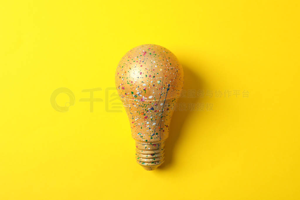 Light bulb with paint splatters on yellow background, space for