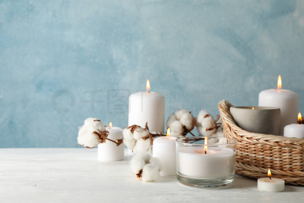 Burning candles, basket and cotton on white wooden table, space