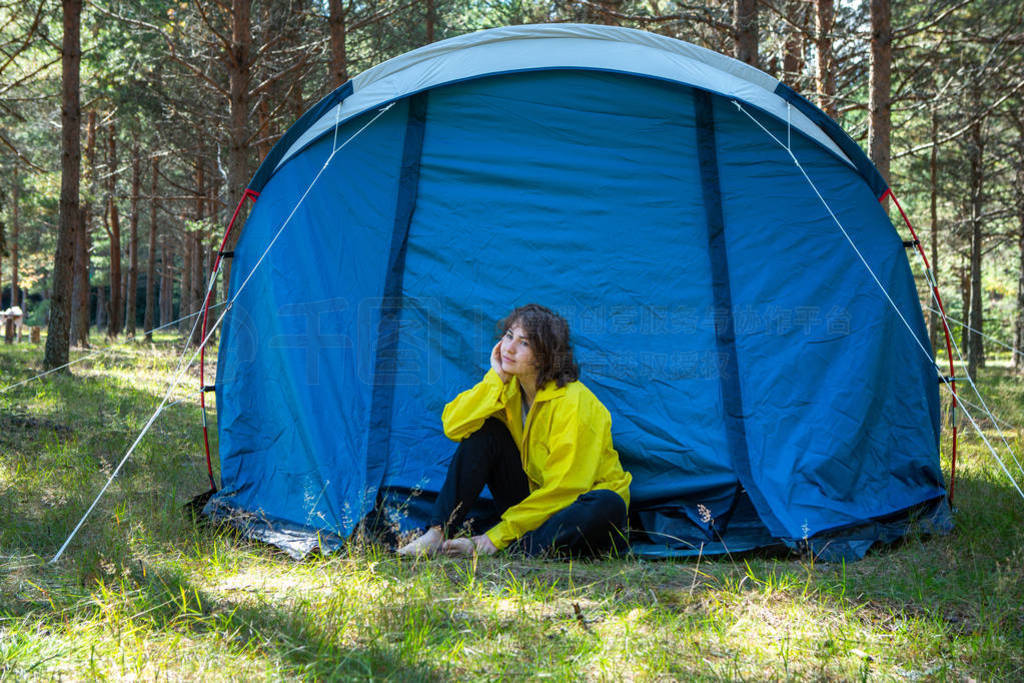 Tourism. A girl in a yellow jacket next to a blue tent.