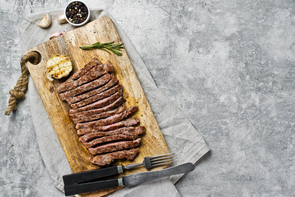 Sliced BBQ steak on wooden chopping Board. Gray background, top