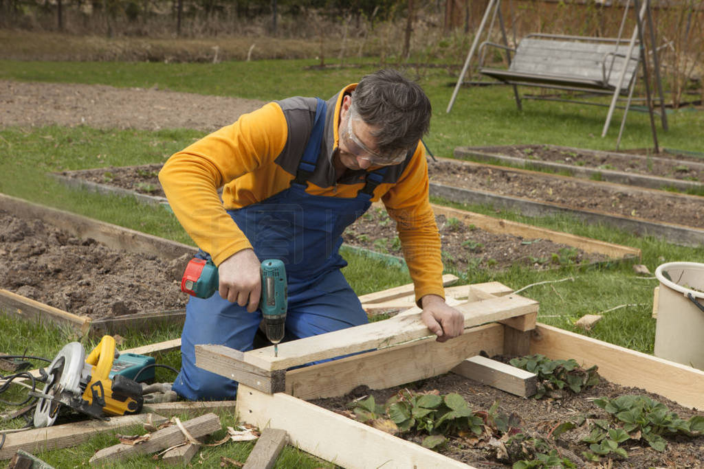 Man on garden plot twists screws into boards