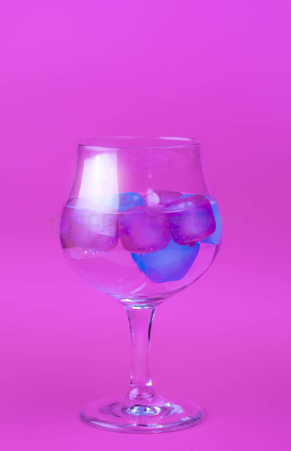 A cold drink with colorful pink and blue ice in a wine glass on