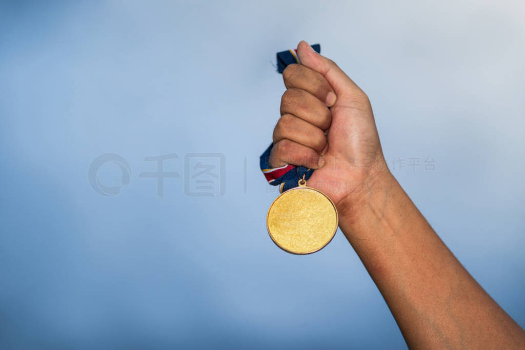 Hand holding gold medal on against cloudy sky background