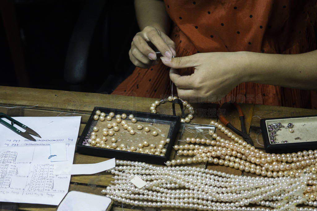 Close hand jeweler stringing pearls on a necklace. Worker in the