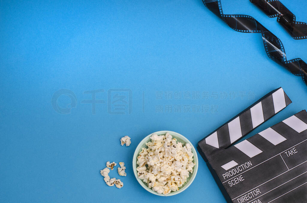 Clapper board with popcorn and film strip on a bright blue backg