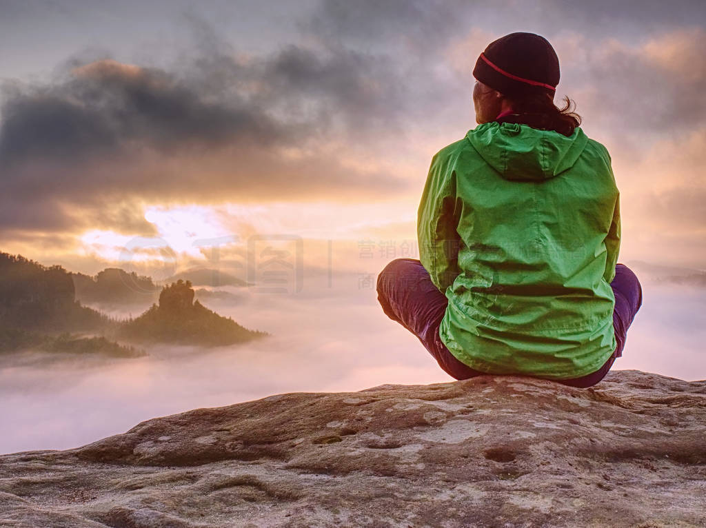 Green jacket woman pensively sitting on the edge of a rock