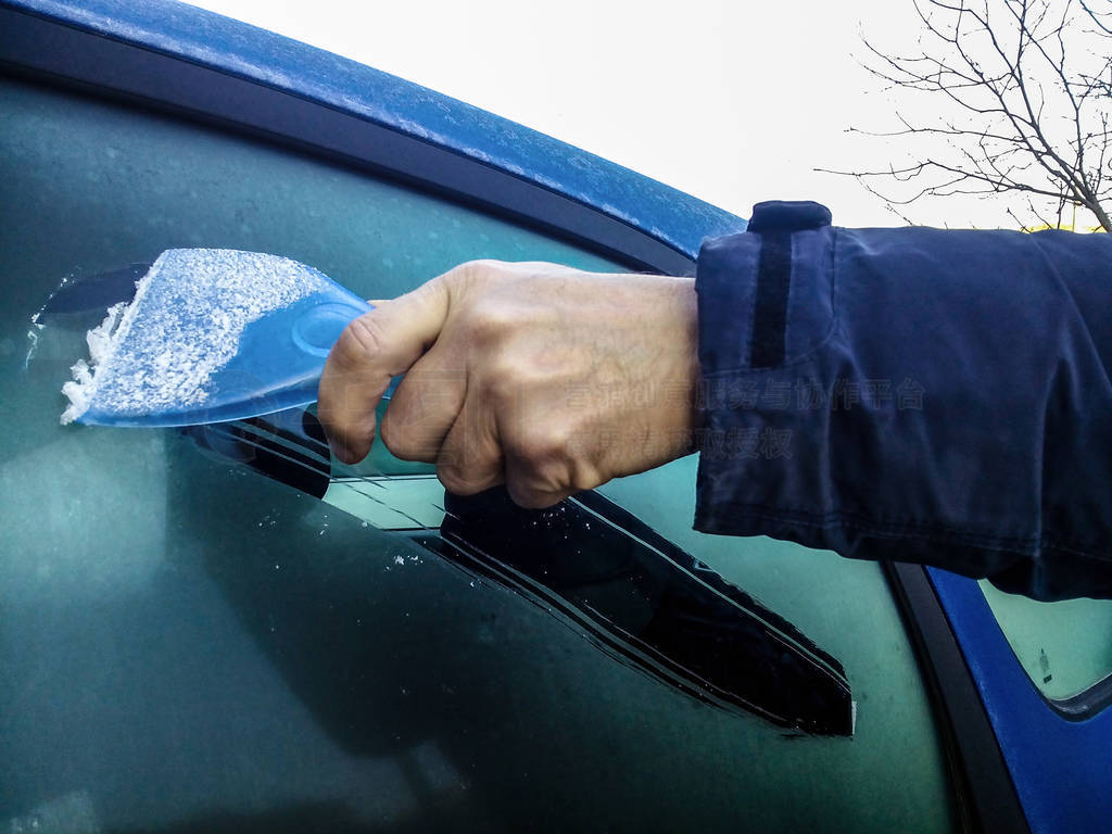A man scrapes hoarfrost with a plastic scraper from the side win