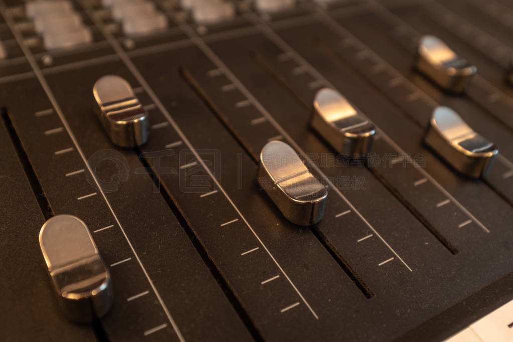 A close up of silver-coloured sliders on a mixing desk in a musi