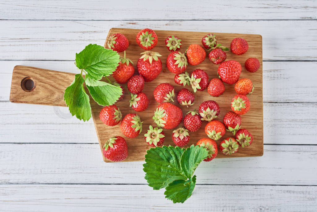 Heap of fresh strawberries with cutting board on a white wooden