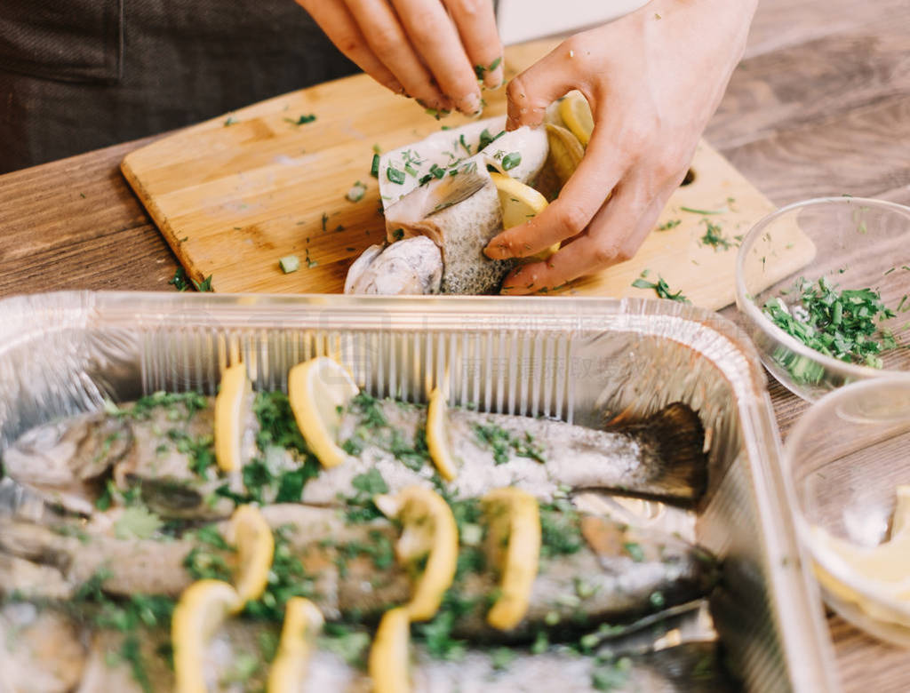 Woman preparing raw fish with lemons and greenery.