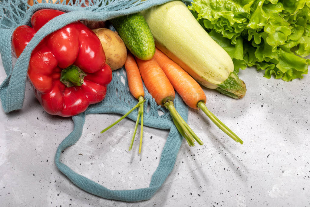 Close-up fresh farm vegetables in string bag on grey concrete ba