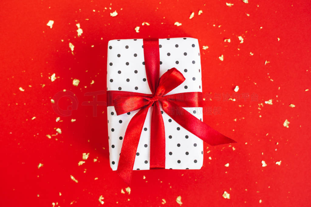 Gift box wrapped in black polka-dot white paper with red bow on