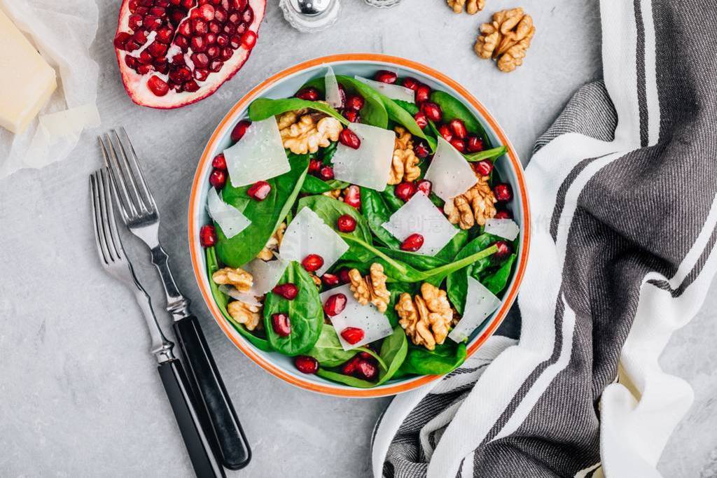 Spinach salad bowl with pomegranate seeds, walnuts and cheese sl
