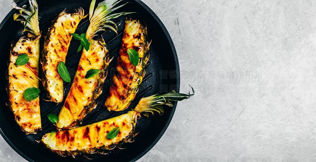 Grilled pineapple with fresh mint in cast iron pan on gray stone