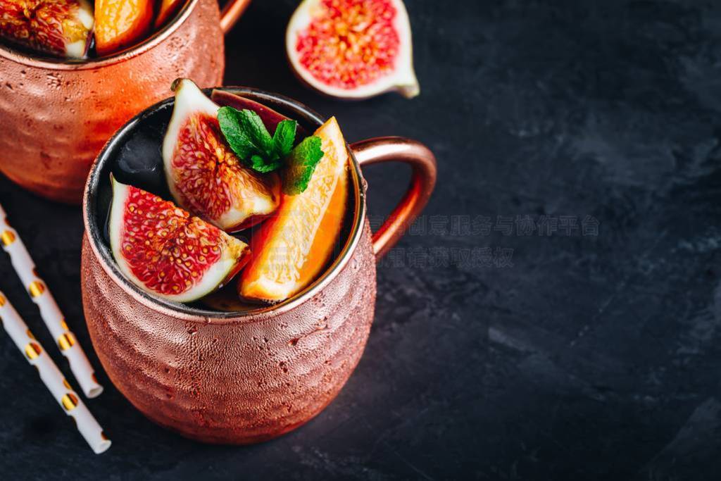 Fig moscow mule ice cold cocktail in copper cup with oranges and